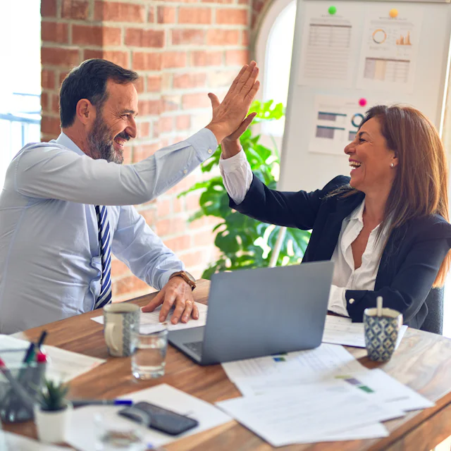 Two colleagues celebrating a successful outcome at a shared desk